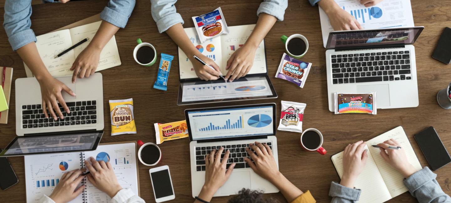 Assorted snacks for college students on a study desk with laptops, notebooks, and tech gear.