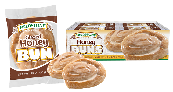 Brown and clear snack package with a glazed honey bun showing through the clear cellophane portion of the wrapping. Two unwrapped honey buns are to the right of the packaged honey bun. A carton is in the background.
